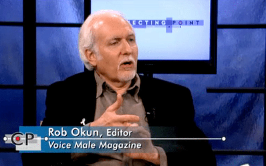 Three men sitting indors in front of a table, talking to each other.