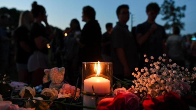 Foreground: candlelit flower memorial for Santa Fe high school. Students silhouetted in background.